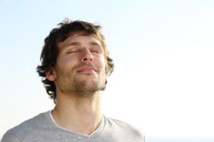 an image of a male practicing mindfulness techniques for recovery while inhaling through his nose with his eyes closed on a white background.