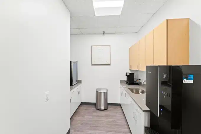 Small kitchen area with white cabinets, stainless steel appliances, and wooden floor.
