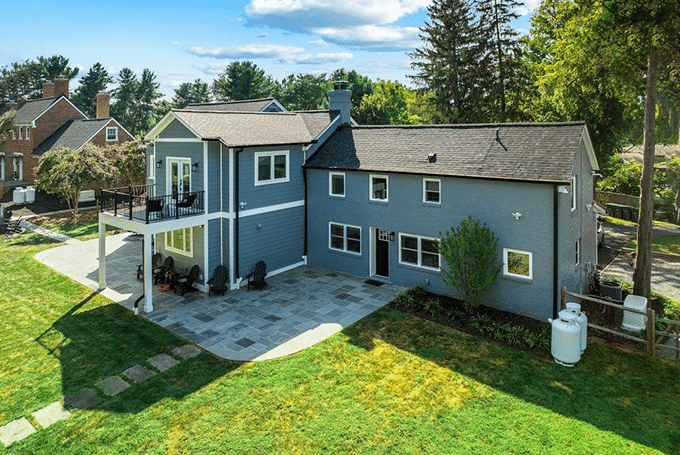 Aerial view of spacious modern home with large patio and garden, surrounded by trees in a suburban neighborhood.