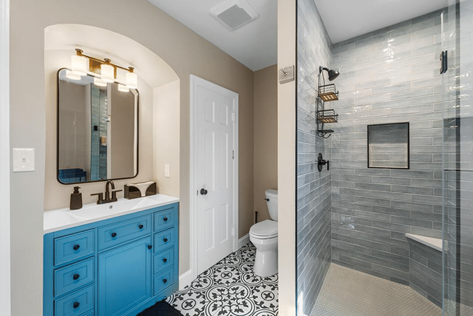 Modern bathroom with blue vanity, patterned floor tiles, and glass shower enclosure showcasing stylish design.